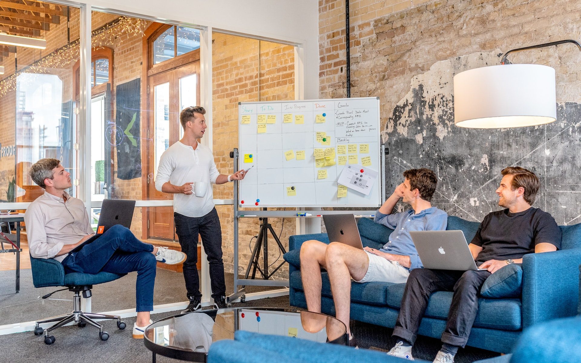 three men sitting while using laptops and watching man beside whiteboard